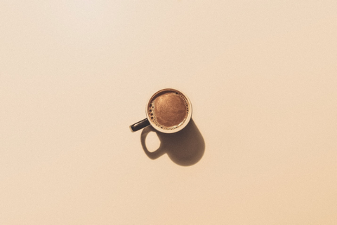 An espresso shot in a mug over a brown background.